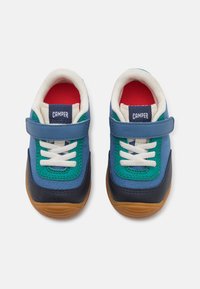 Bunt gefärbte Kindersneaker in Blau, Grün und Marineblau mit weißen Schnürsenkeln, Klettverschluss und einer strukturierten Gummisohle.