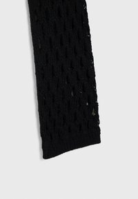 Tissu tricoté noir avec un motif de tissage lâche et ouvert et un bord côtelé, présenté sur un fond clair uni.