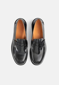 Μαύρο δερμάτινο λουστρίνι με λεία υφή, ραφές και διακοσμητική ζώνη μπροστά. Αντίσταση στην ολίσθηση.