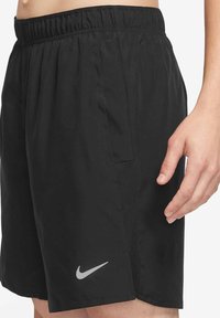 Czarne sportowe spodenki z elastycznym pasem, bocznymi kieszeniami i oddychającą siatkową wstawką. Na dole znajduje się szare logo Nike.