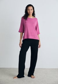 Rosa, lös passande topp med vida ärmar, i kombination med svarta, raka byxor. Mjuk textur, minimalistisk design mot en neutral bakgrund.