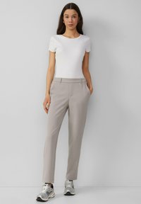 Beige op maat gemaakte broek met een rechte snit, met een gladde textuur en zijzakken, gecombineerd met een uitstrakkervormig wit ribbeltopje en sneakers.