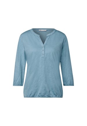 Lyseblå langærmet bluse med rund krave og fire knapper ved halsen. Blød tekstur med en let glans. Elastisk detail ved taljen.