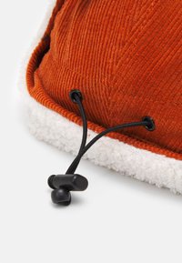 Orange corduroy fabric with white faux shearling trim. Features black drawstring hardware for adjustment. Textured and durable material.