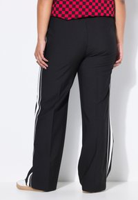Zwarte wijde broek met witte zijstrepen, met een gladde textuur en een elastische tailleband. De achterkant toont een gestroomlijnd ontwerp.