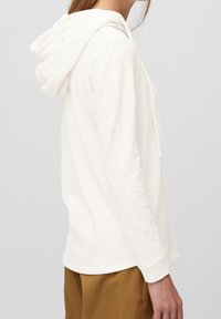 Sudadera color beige claro en un tejido suave y texturizado; presenta una vista lateral con capucha ajustable, corte relajado y mangas largas.