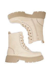 Beżowe skórzane buty militarne z grubą, żłobioną podeszwą, bocznym zamkiem błyskawicznym oraz dekoracyjnymi srebrnymi ćwiekami wzdłuż strefy sznurowania.