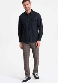 Camisa de botones color navy con dos bolsillos en el pecho, combinada con pantalones de cuadros marrones y zapatillas azules con suelas y cordones blancos.
