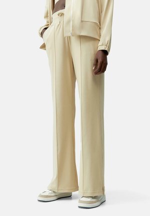 Beige wide-leg pants made of soft fabric, featuring an elastic waistband and subtle stitching details, worn with light-colored sneakers.