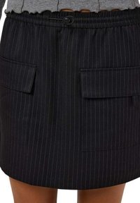 Jupe noire à rayures, fabriquée dans un tissu avec une taille élastique et un cordon de serrage. Dispose de deux poches avant pour plus de fonctionnalité.