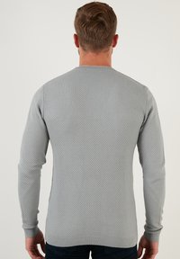 Maglione grigio lavorato a maglia con un motivo testurizzato, maniche lunghe e polsini a costine, mostrato da dietro su uno sfondo semplice.
