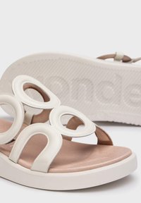 Sandalias blancas con recortes circulares y tiras suaves, que presentan una plantilla de color beige suave y una suela blanca texturizada.