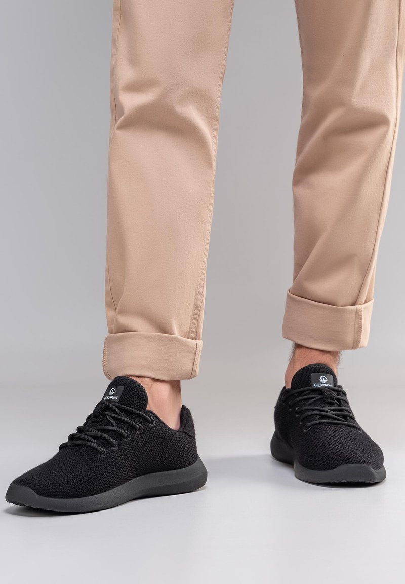 Baskets légères noires à tige en mesh, bout rond et semelle en caoutchouc plate, associées à un pantalon beige clair retroussé.