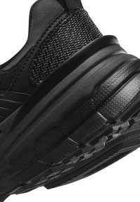 Black athletic shoe featuring a textured mesh upper, smooth synthetic accents, and a thick, patterned rubber outsole for traction.