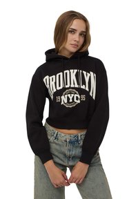 Felpa nera corta con testo "BROOKLYN NYC 1995". Caratterizzata da cappuccio con coulisse e polsini a costine, abbinata a jeans azzurri a vita alta.