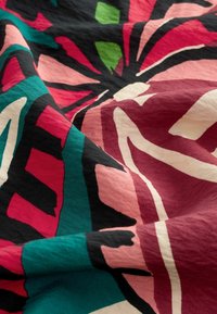 Tkanina z żywym, abstrakcyjnym kwiatowym wzorem w kolorach czerwonym, różowym, zielonym, czarnym i kremowym, ukazująca fałdy i szczegóły tekstury.