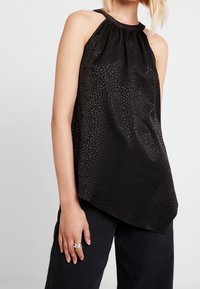 Svart ärmlös topp med ett strukturerat mönster, med en samlad halsringning och en asymmetrisk kant, tillverkad av lätt material.