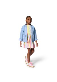 Veste en jean bleu clair à coupe oversize, portée sur une robe à rayures pastel. Les chaussures sont roses et beiges avec des lacets.