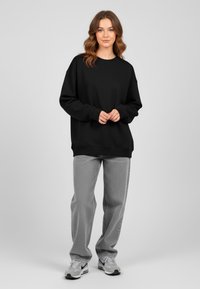 Felpa nera over-size con polsini a coste, abbinata a jeans dritti grigio chiaro e scarpe da ginnastica grigie. Tessuto liscio con vestibilità comoda.