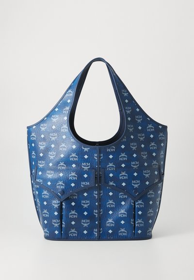 Blaue Leder-Umhängetasche mit MCM-Logo-Muster, ausgestattet mit zwei Taschen mit Klappe an der Vorderseite und einer breiten Öffnung für den Griff.