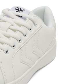 Vit syntetiska sneakers med en slät yta, prydda med dekorativt chevronmönster, vita snören och en vadderad krage.