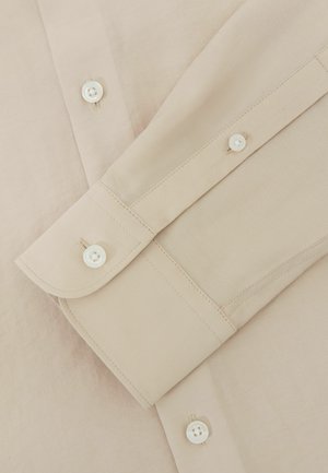 Beiges Langarmhemd mit Nahaufnahme der geknöpften Manschetten und Vorderknöpfe auf glattem Stoff.