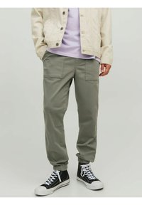 Pantaloni cargo leggeri color oliva con polsini elastici, due tasche frontali e una vestibilità comoda, abbinati a una maglietta lilla e un giubbotto crema.