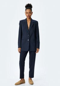Marynarski blazer w paski oraz pasujące spodnie wykonane z lekkiego materiału, z dwoma guzikami, otwartymi klapami i kieszeniami bocznymi. Brązowe mokasyny.