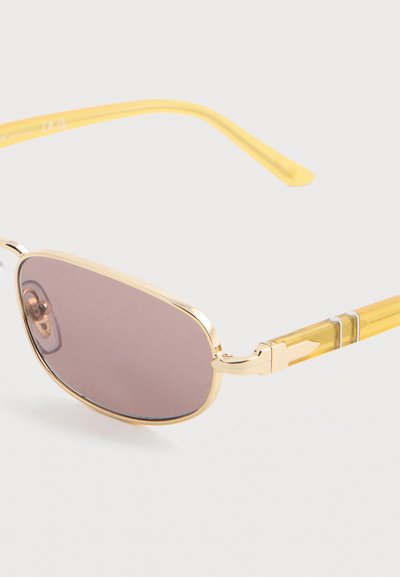 Γυαλιά ηλίου με χρυσή κορνίζα, ορθογώνιους φακούς με μωβ απόχρωση και διάφανα κίτρινα σκέλη, σε λευκό φόντο.