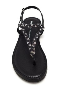 Sandalia tipo thong negra con una cinta trenzada que presenta detalles en plata, plantilla texturizada y suela plana. Correa ajustable en el tobillo para un mejor ajuste.