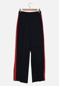 Pantalons larges noirs avec des bandes rouges sur les côtés, détails zippés au niveau des ourlets, en tissu lisse, taille haute et coupe ample.