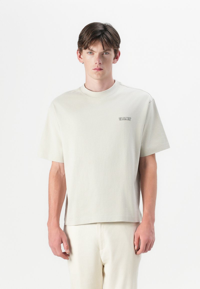 Helles beige T-Shirt mit kurzen Ärmeln und Rundhalsausschnitt, bestickt mit dem Logo "SELECTED" in dezentem Farbton. Weiches Baumwollmaterial, lockere Passform.