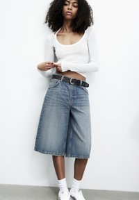 Culotte in denim di colore azzurro chiaro, a vita media con orlo sfilacciato, abbinate a una maglietta bianca a maniche lunghe e una cintura nera con hardware in argento.