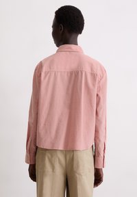 Cropped pink shirt made of lightweight fabric, featuring long sleeves and buttoned cuffs, with a clean back design and soft texture.