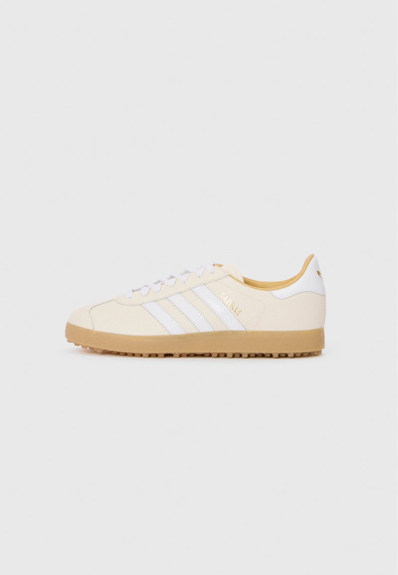 Witte en crèmekleurige sportschoenen met drie witte strepen en gouden branding. Heeft een gestructureerde bovenkant en een gumrubberen zool met kleine noppen.