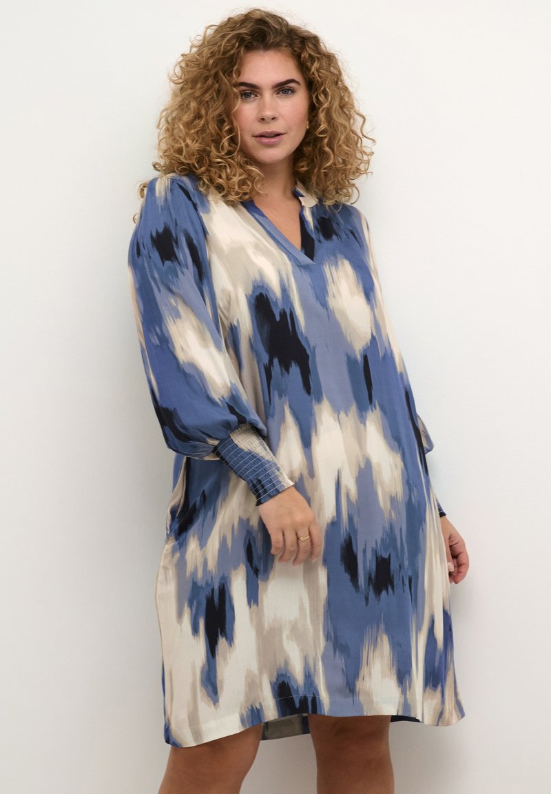 Robe à motifs bleus, crème et noirs avec un décolleté en V, des manches longues et des poignets froncés. Tissu lisse avec une coupe décontractée.