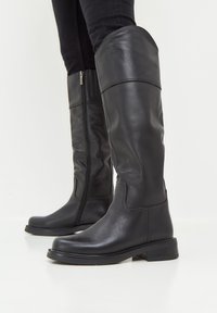 Black leather knee-high boots with side zippers, rounded toes, and a low block heel. Smooth texture with minimal stitching details.