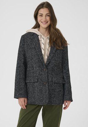Sacou cu model pe herringbone în alb și negru, cu o croială ajustată, două butoane și buzunare laterale, purtat peste un hanorac bej.