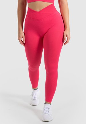 Růžové legíny s vysokým pasem, vyrobené z elastického žebrovaného materiálu. Nosené s bílými sportovními botami s černými akcenty.