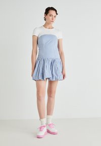 Robe en vichy bleu et blanc avec un corsage ajusté et une jupe évasée, associée à des chaussures blanches avec des semelles et des lacets roses. Tissu en coton doux.