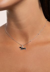 Collana in argento con un pendente a forma di dachshund smaltato di nero con contorni bianchi, appoggiato su un collo di tonalità della pelle.