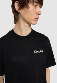 Černé bavlněné tričko s kulatým výstřihem. Na levé straně hrudi se nachází bílé logo. Krátké rukávy, volný střih a měkká textura.