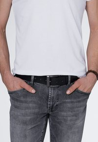 Black leather belt with a silver metal buckle, worn with gray denim jeans and a white t-shirt. Notable stitching on the jeans.