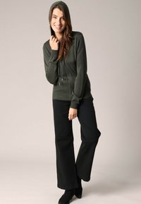 Donkergroene sweatshirt met capuchon en koordjes, van een gestructureerde breimateriaal, gecombineerd met zwarte wijde broek en zwarte enkellaarsjes.