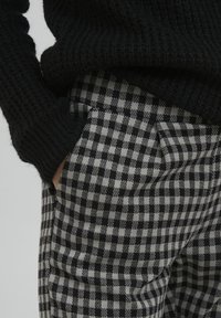 Zwarte gebreide trui met ribbelstructuur, gecombineerd met grijs en zwart geruite broek met een zijzak.