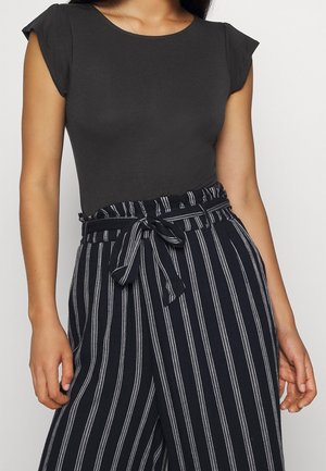 Femme portant un haut noir ajusté à manches courtes associé à un pantalon bleu marine taille haute avec des rayures verticales blanches et une ceinture nouée.