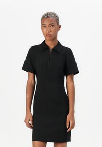 Black polo dress with short sleeves, featuring a front zipper and structured fit. Smooth fabric and two side pockets for detail.