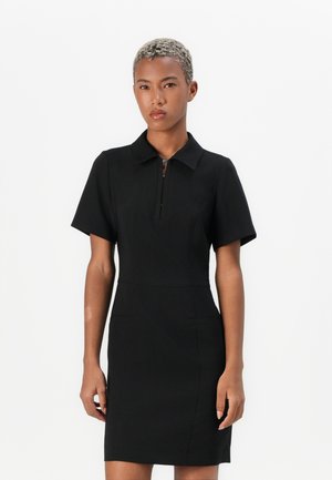 Black polo dress with short sleeves, featuring a front zipper and structured fit. Smooth fabric and two side pockets for detail.