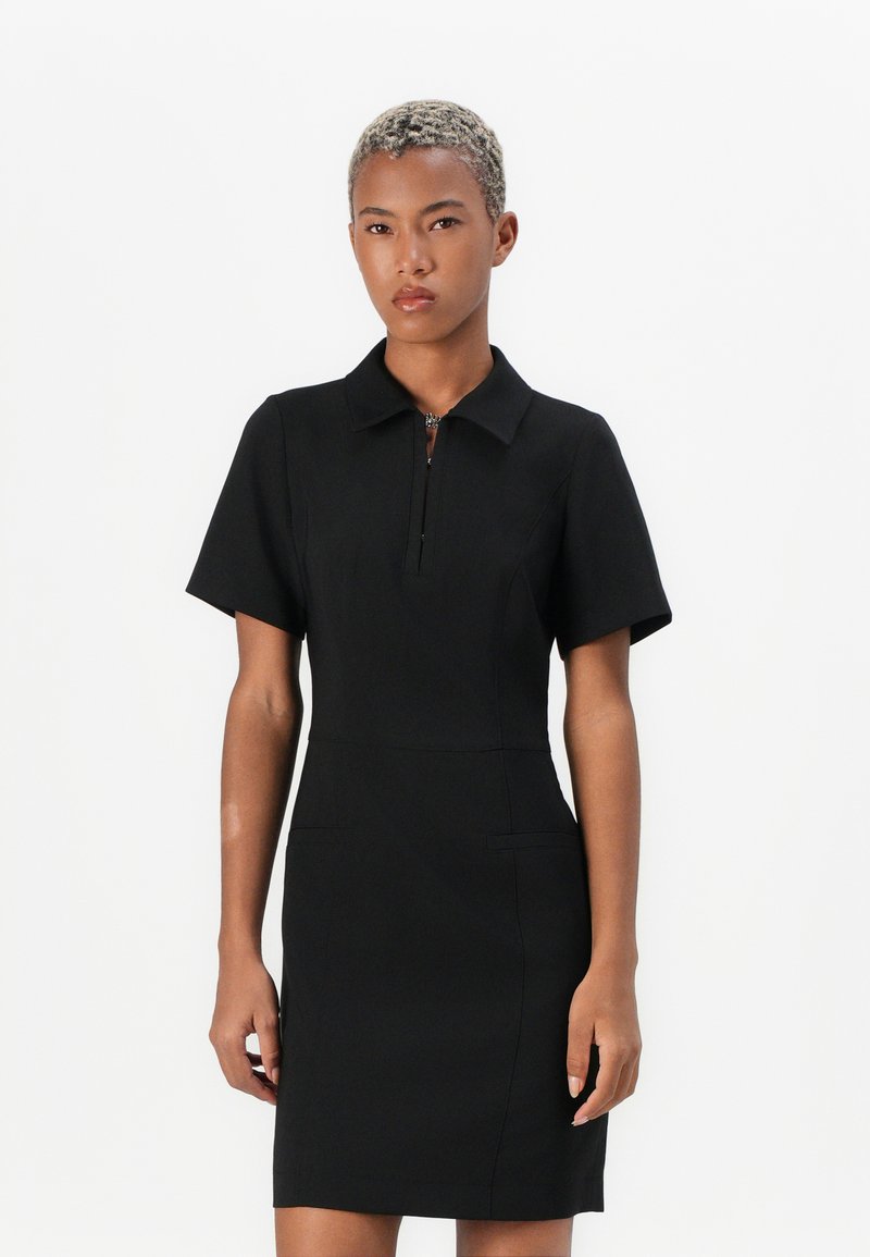 Black polo dress with short sleeves, featuring a front zipper and structured fit. Smooth fabric and two side pockets for detail.