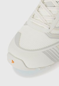 Weißer Sportschuh mit Obermaterial aus Mesh, grauen Akzenten, strukturiertem Profil und orangefarbenem Logo-Detail nahe der Ferse. Mit Schnürsenkeln oben.